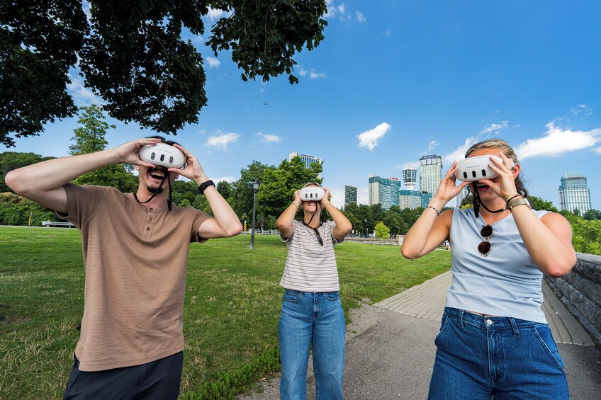 Three people wearing virtual reality headsets in a park with a city skyline in the background. 2