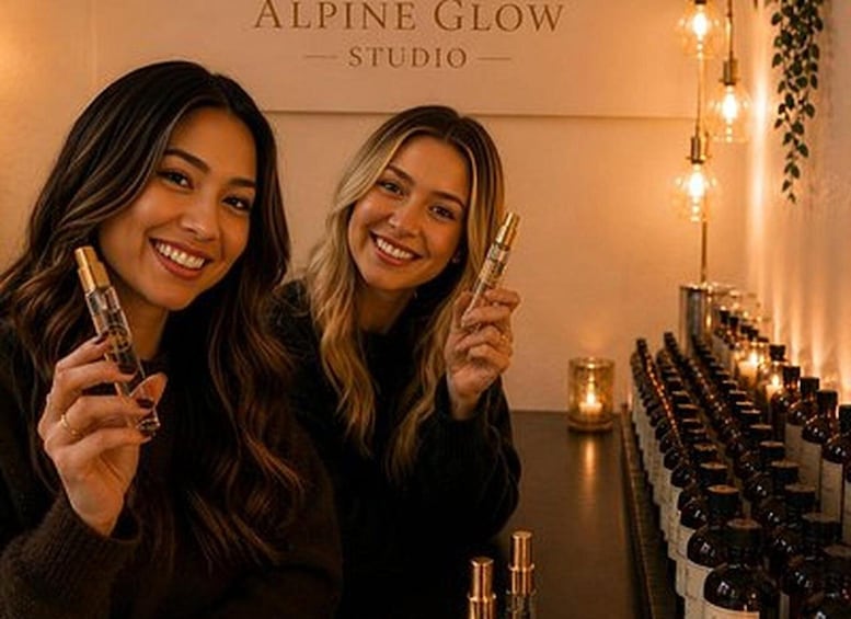 Two individuals holding products in a room with a wall sign reading 'ALPINE GLOW STUDIO' and bottles lined up on a counter. 2