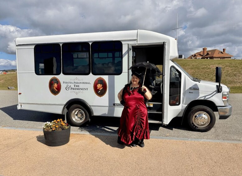 A white van with 'Pirates, Paranormal, The Prominent' branding parked on a road with a woman in a red dress standing beside it. 5