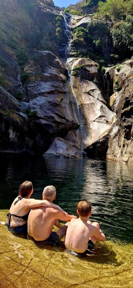 A waterfall, rocky terrain, and a group of people sitting by a clear water body. 3