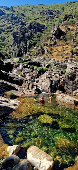 A clear mountain stream with people swimming and a waterfall in the background. 5