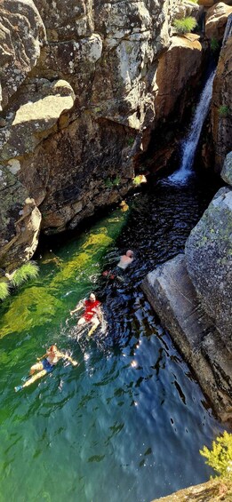 A natural pool with a waterfall, surrounded by rocky terrain and greenery. 2