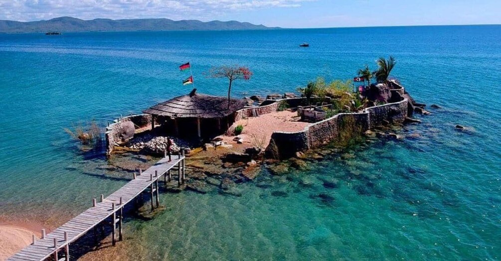 A coastal island with clear waters, a wooden pier, and a small hut with flags. 5