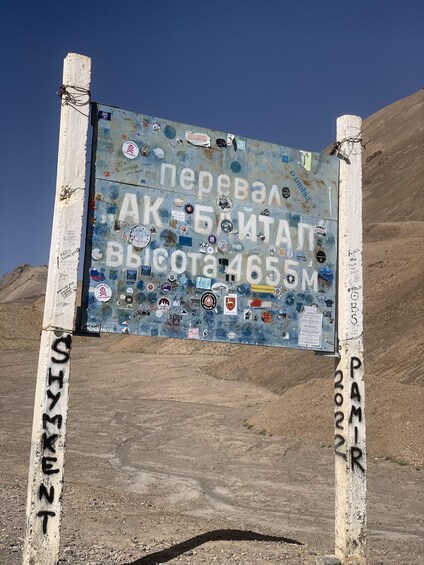 A weathered sign with stickers and graffiti, surrounded by a barren landscape. 2