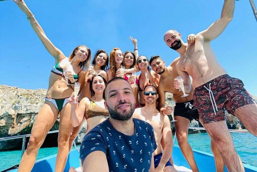A group of people on a boat with clear blue water and rocky cliffs in the background. 5