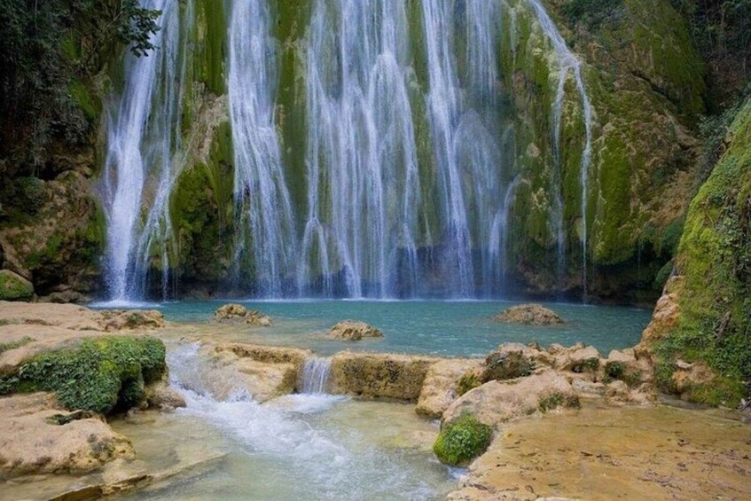 A waterfall cascading into a clear pool surrounded by moss-covered rocks. 1