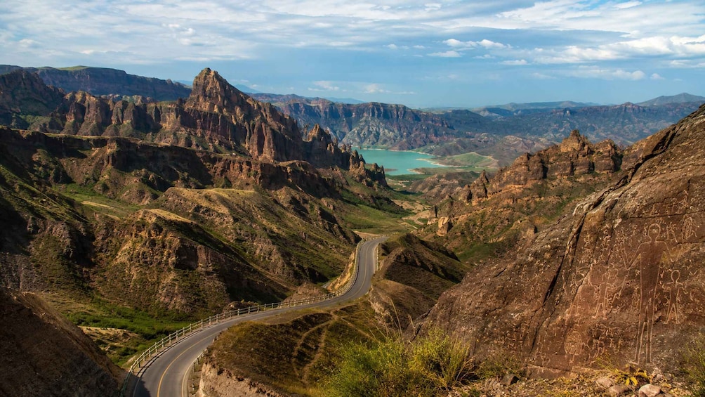 A winding mountain road with rocky terrain and a distant turquoise lake. 4