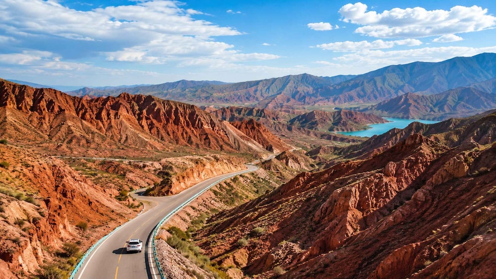 A winding road through a mountainous landscape with a lake in the distance. 1