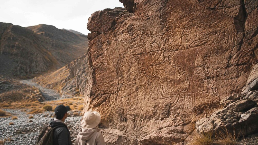 Two people observing a large rock formation in a mountainous area. 5