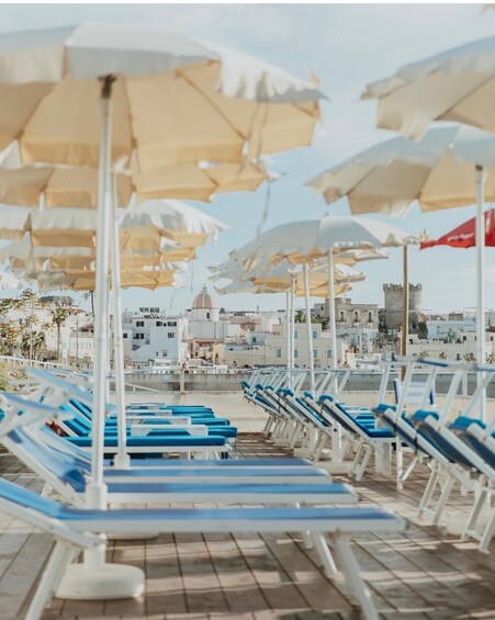 A beachside lounge area with rows of blue and white sun loungers and beige umbrellas. 2