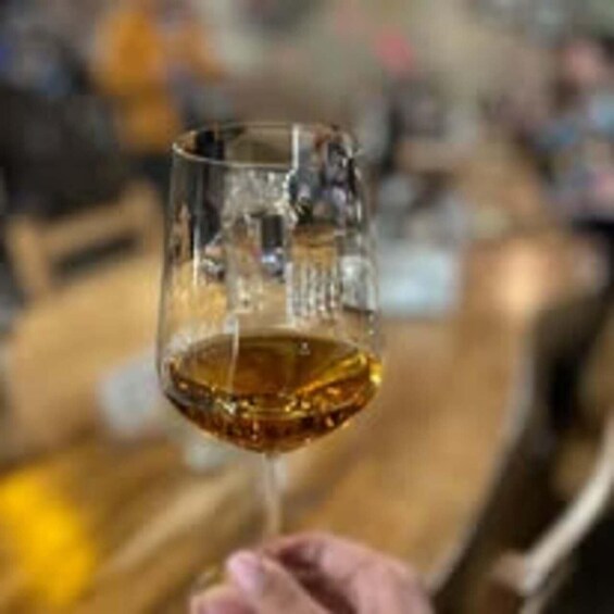 A close-up of a glass of amber liquid, likely a beverage, held by a person. 4