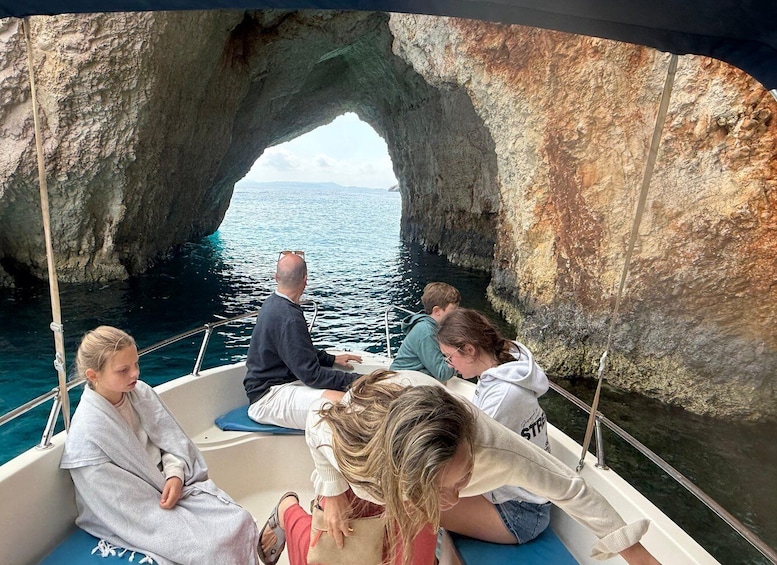 A boat passing through a natural rock arch with clear blue water and distant land visible. 2