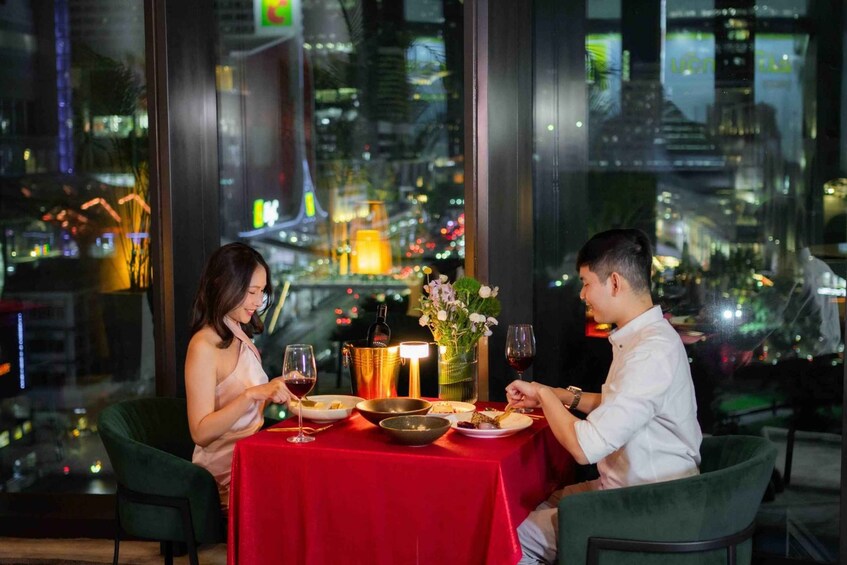 Two people dining at a table with a red tablecloth, city lights in the background, and a view of the cityscape. 3