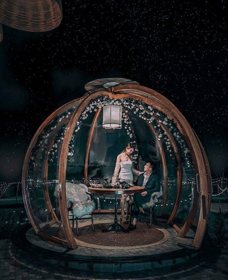 A gazebo with a glass dome, a table, and chairs inside, surrounded by a garden. 2