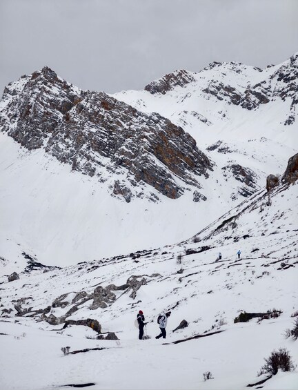 A snowy mountain landscape with rocky outcrops and two hikers in the foreground. 5
