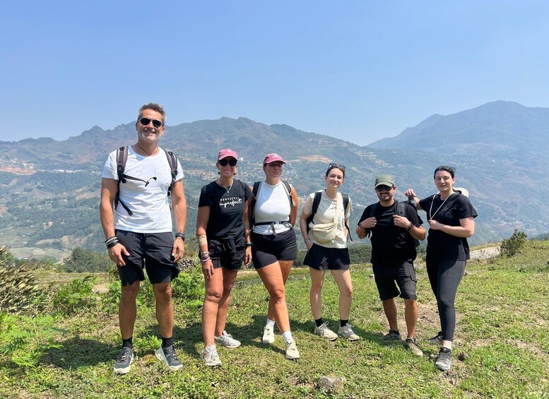 A group of people standing on a grassy hill with a mountainous landscape in the background. 1