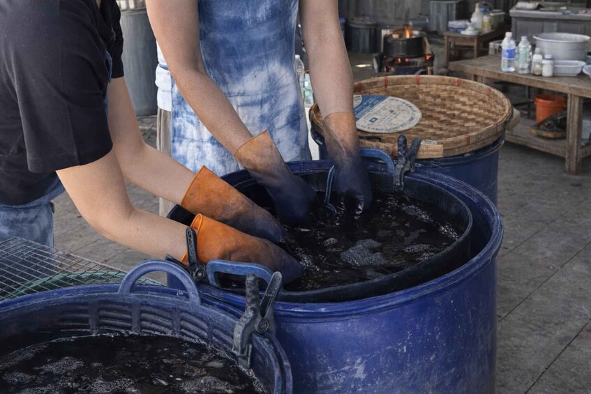 Two people handling a large blue container with a basket on top, in an outdoor setting with tables and containers in the background. 4