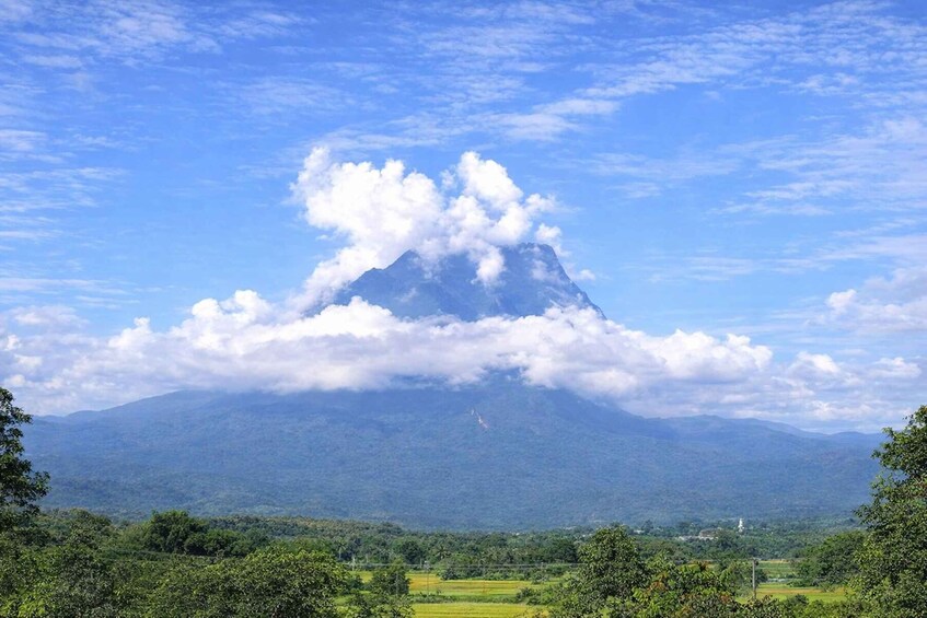 A mountain with a cloud formation at its peak, surrounded by lush greenery and a clear blue sky. 3