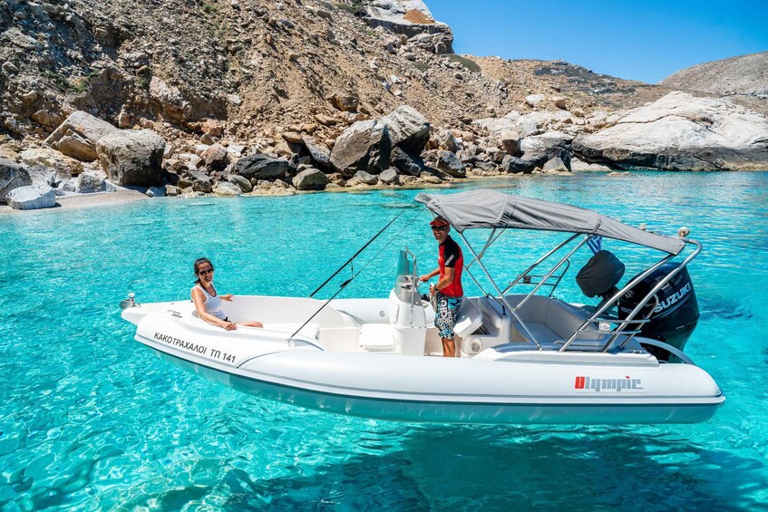A white inflatable boat with 'Olympic' branding on the side, two people on board, and clear turquoise water. 5