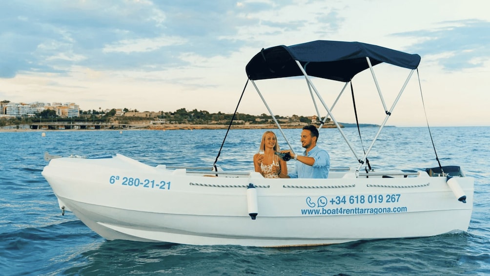 A white boat with a canopy, a man and a woman on board, and a coastal cityscape in the background. 3