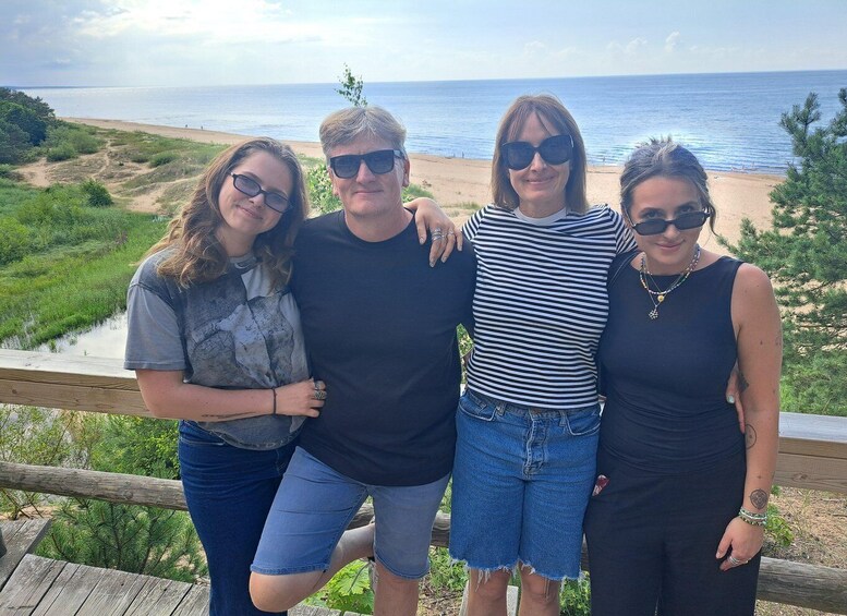 Four people standing on a wooden deck overlooking a beach with a clear view of the ocean. 5