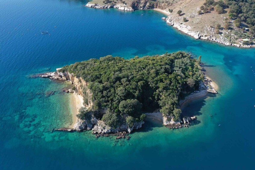 An aerial view of a small island with clear turquoise waters, surrounded by rocky coastlines and dense green forests. 3