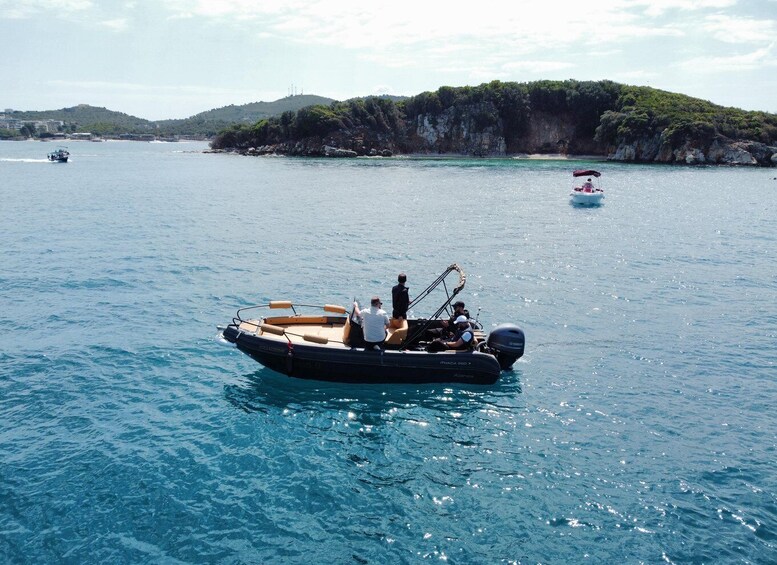 A small motorboat on calm blue waters with a rocky coastline and hills in the background. 4