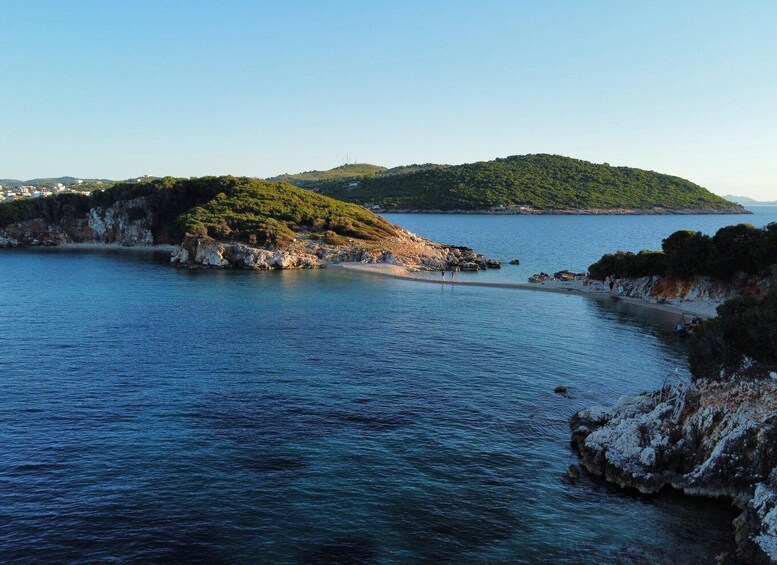 A coastal landscape with a small island covered in greenery, calm blue waters, and rocky shores. 1