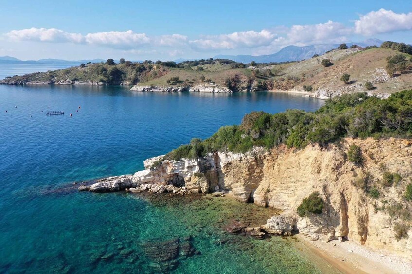 A coastal landscape with clear blue waters, rocky cliffs, and distant mountains. 5