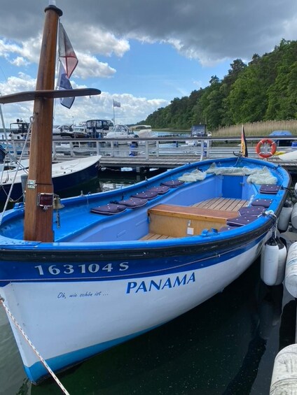 A blue and white boat named 'PANAMA' docked at a marina with other boats and a forested hill in the background. 2