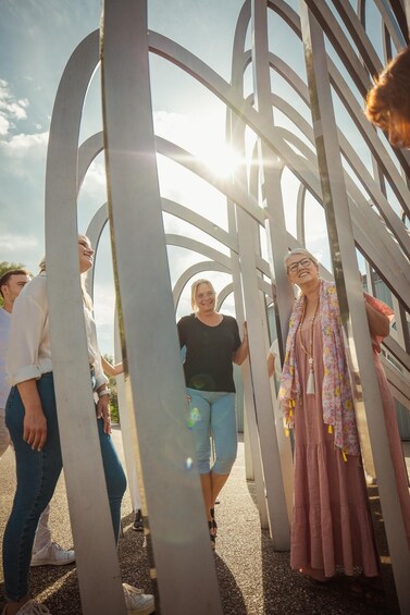 People standing in front of a metal sculpture with a sunlit sky in the background. 2