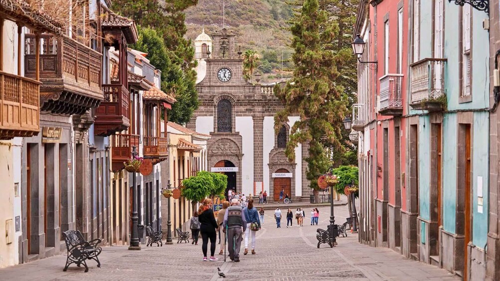 A cobblestone street lined with historic buildings, a church with a clock tower, and people walking. 3