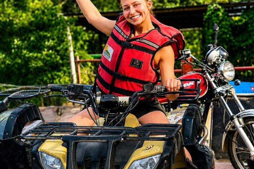 A person riding an ATV with a red life jacket, surrounded by greenery. 1