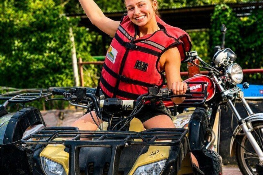 A person riding a quad bike with a yellow and black color scheme, wearing a red life jacket, and a helmet. 1