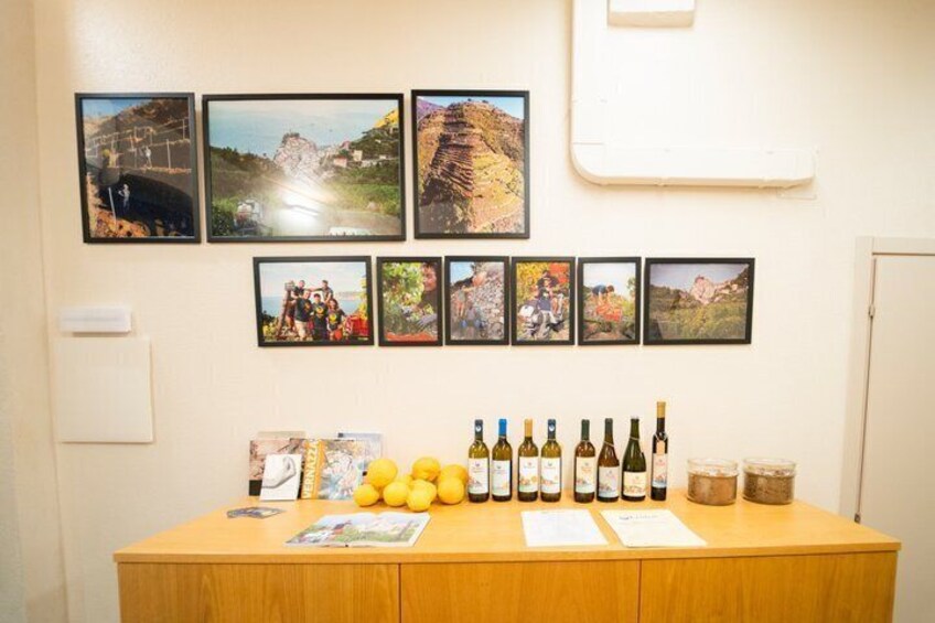 A wooden counter with wine bottles and lemons, and a wall with framed pictures. 5