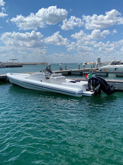 A white motorboat docked at a marina with a clear blue sky and scattered clouds in the background. 1