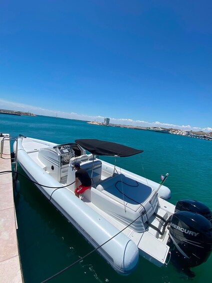 A white inflatable boat docked at a marina with a clear blue sky and a distant shoreline. 2