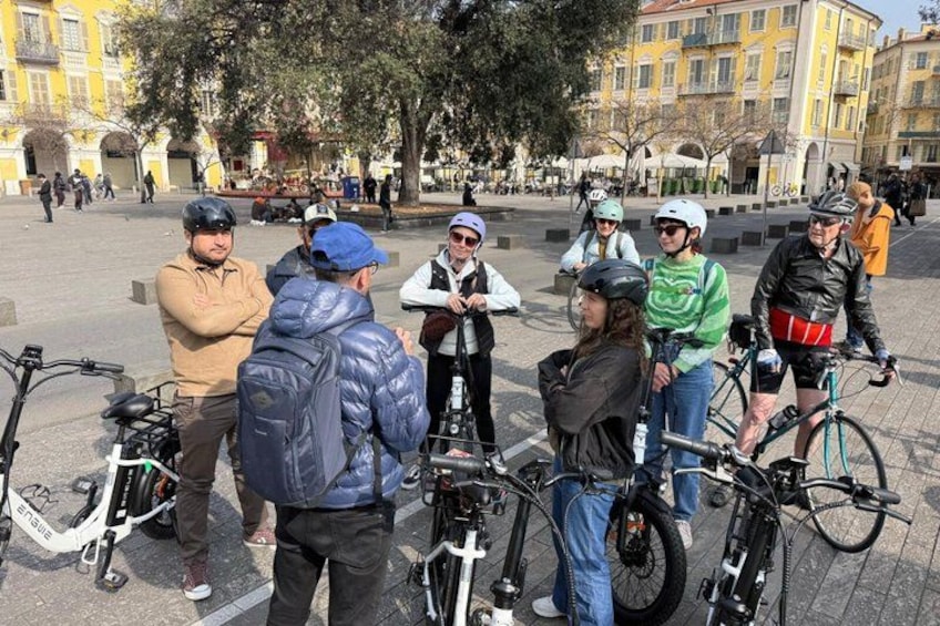 A group of people with bicycles in an urban square. 1