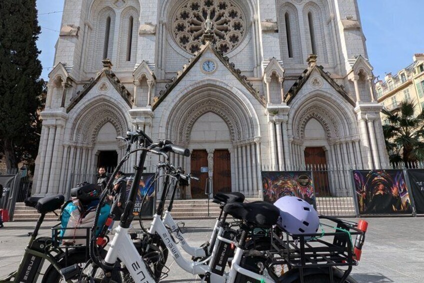 A white church with Gothic architecture, a bicycle, and a person sitting on a bike. 1