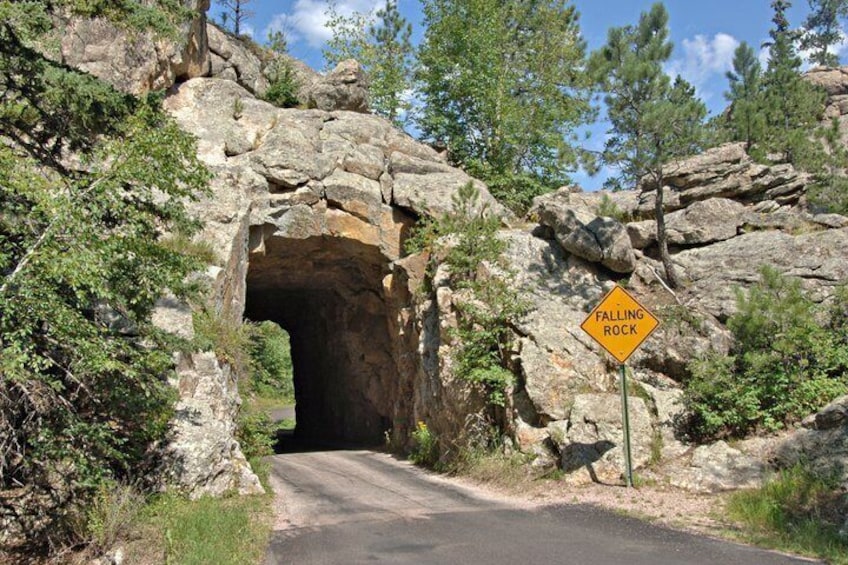 A road passing through a rocky tunnel with a 'Falling Rock' warning sign. 2