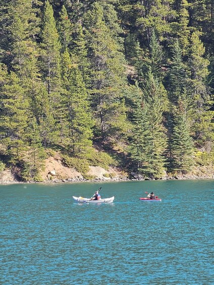 Two kayakers on a calm lake surrounded by dense forest. 2
