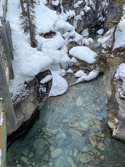 A snow-covered stream with clear water flowing through a rocky gorge. 5