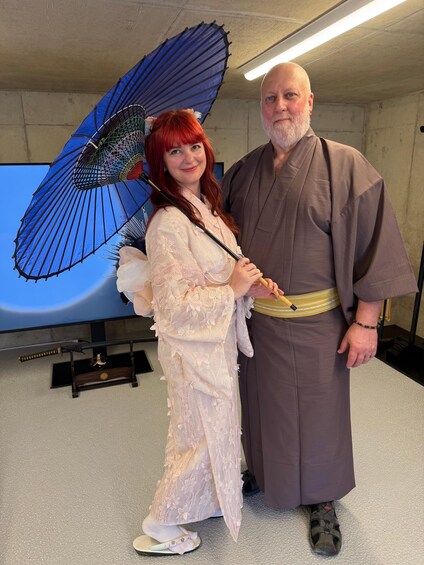 Two people in traditional attire, one holding a blue fan. 1