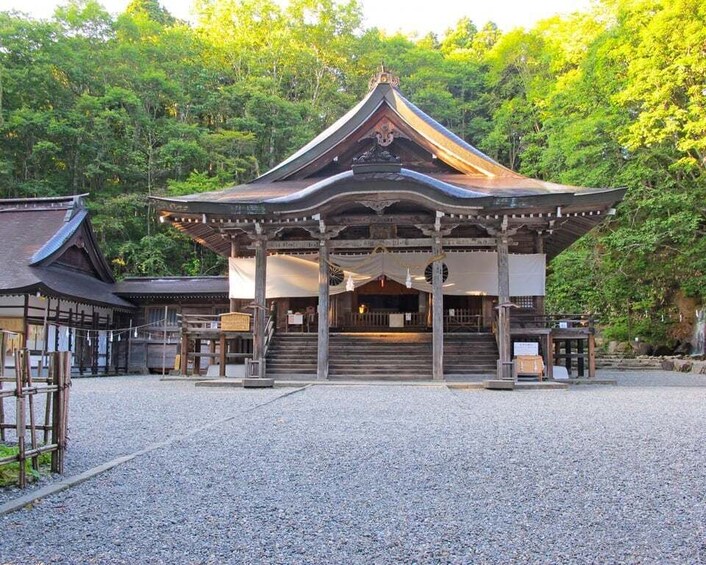 A traditional Japanese temple with a curved roof, surrounded by a gravel courtyard and dense forest. 2