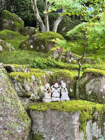 Un jardín tranquilo con rocas cubiertas de musgo y tres estatuas de piedra. 2