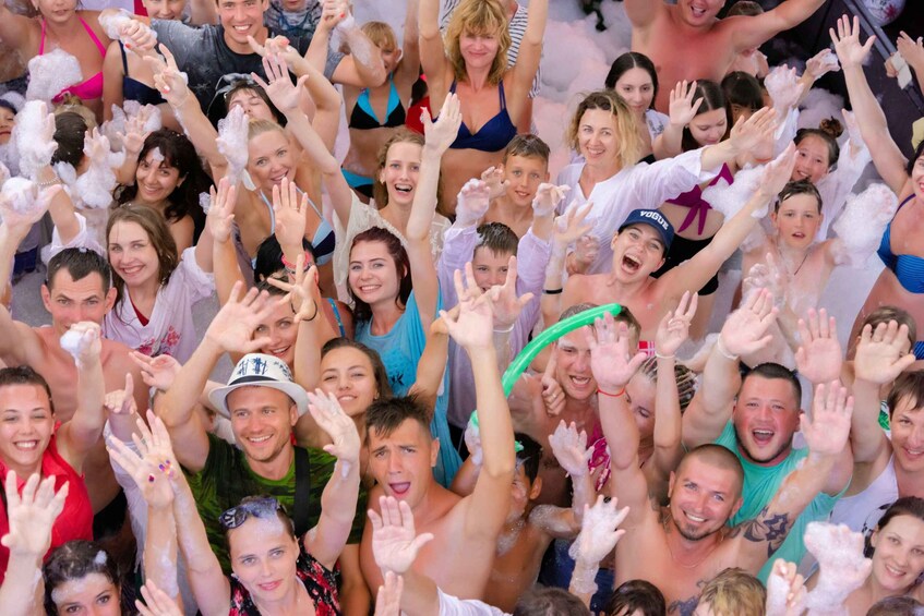 A crowd of people with raised hands, some wearing hats, and a green inflatable tube. 5