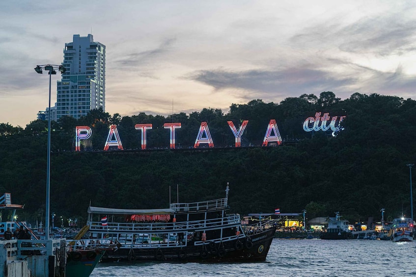 A boat docked at a waterfront with illuminated letters spelling 'PATTAYA' in the background. 3