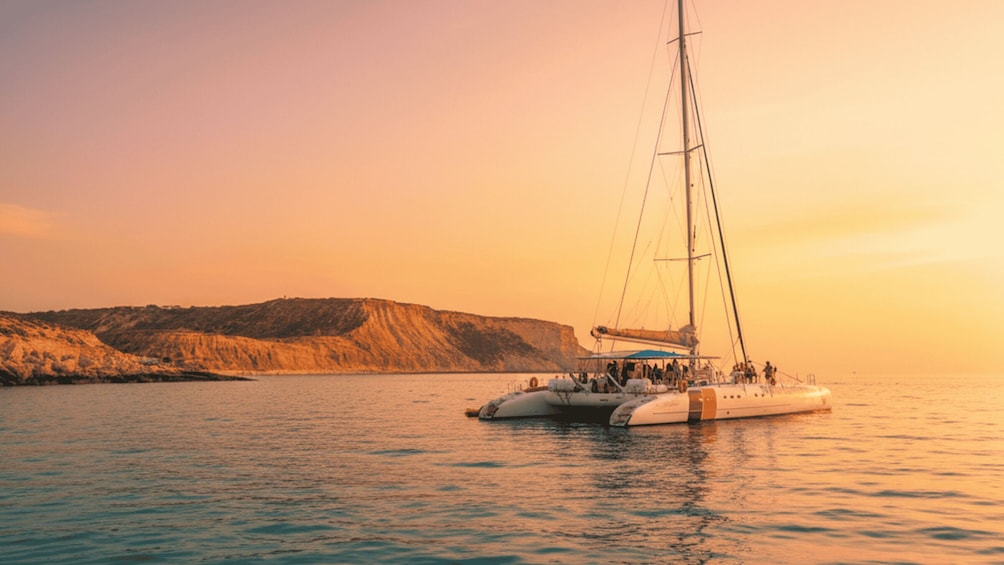 A sailboat on calm waters with a hilly coastline in the background. 1
