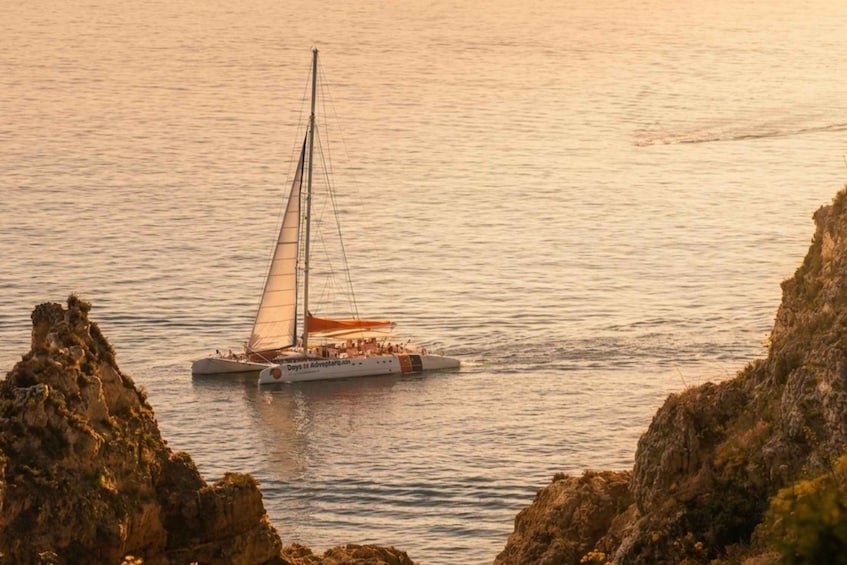 A sailboat on calm waters with rocky cliffs in the foreground. 2