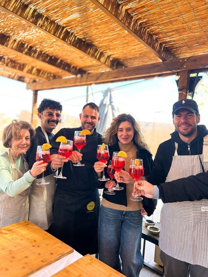 A group of people toasting with red drinks at an outdoor setting with a wooden ceiling. 1